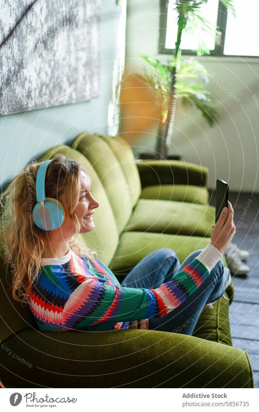 Young woman relaxing with headphones and smartphone sofa green cheerful music technology young break room light-filled nature-inspired aesthetic indoor leisure