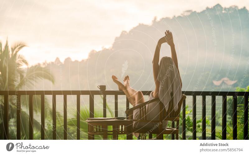 Woman enjoying a peaceful morning in a tropical setting woman balcony stretching sunrise tranquility rejuvenation landscape mist lush relaxed natural scenic