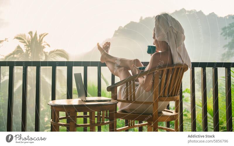 Woman relaxing with coffee on tropical balcony at sunrise woman morning landscape mist rustic peace towel laptop sitting enjoying scenery nature serene comfort