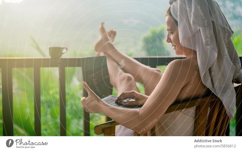 Woman relaxes with laptop on scenic balcony woman towel coffee cup greenery serene morning relaxing summer outdoor leisure tranquil technology internet browsing