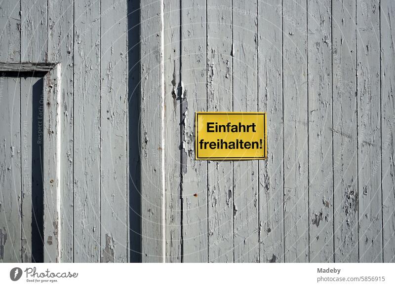 Old wooden barn door in pastel colors of an old farm with yellow sign Keep driveway clear in sunshine in Wettenberg Krofdorf-Gleiberg near Gießen in Hesse Sign