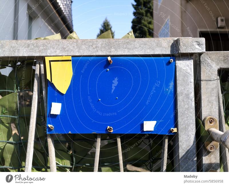 Blue plastic plaque with remnants of a yellow sign on the gate of a home in the sunshine in Oerlinghausen near Bielefeld on the Hermannsweg in the Teutoburg Forest