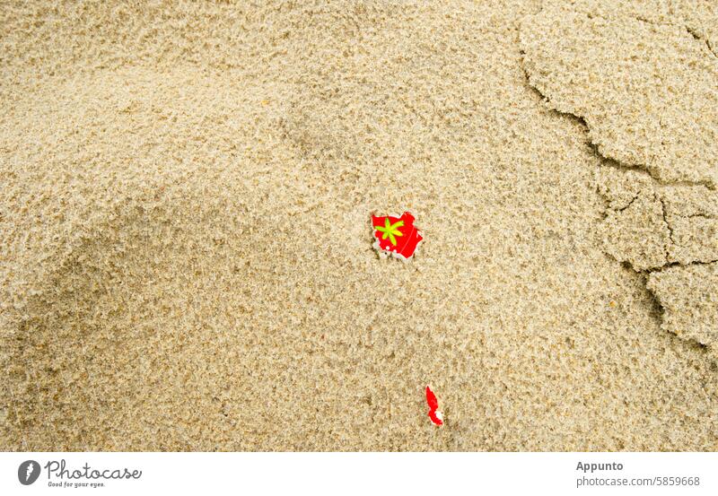 Beach snippets on the beach of dreams - Small red paper snippets lie on a sandy beach. On one of them you can see a stylized green plant, which could be a palm tree or a hemp plant; symbolic image