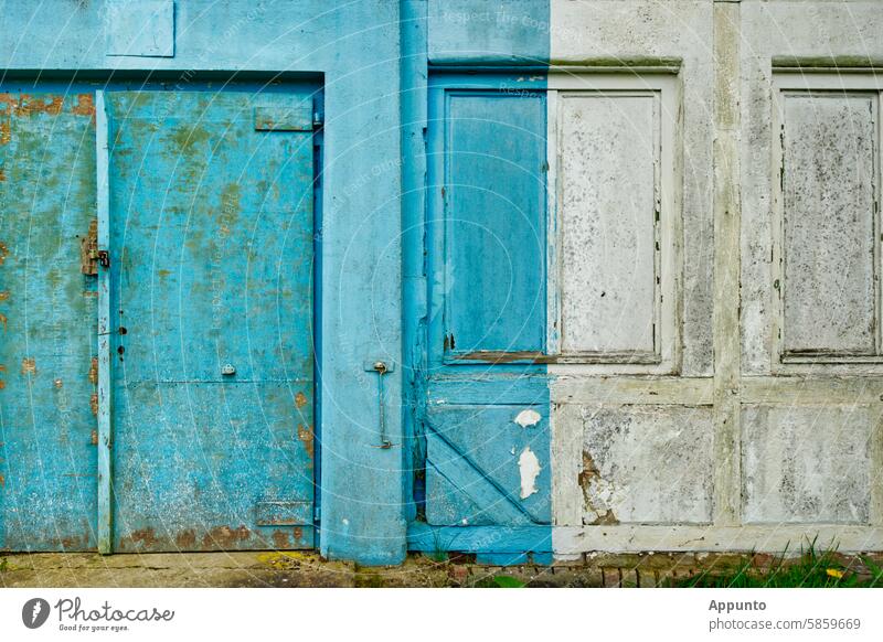Section of a weathered exterior wall of a building with an old, partially rusted steel door and a vertically divided coat of paint partly in light turquoise blue and partly in white