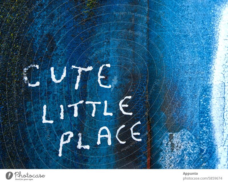 "Cute little place" - Handwritten, three-line lettering in white capital letters on a deep blue metallic background with traces of rust and white paint