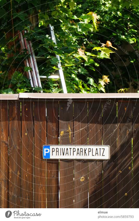 Sign P PRIVATPARKPLATZ on a brown wooden fence in front of a maple tree with ladder Parking lot private parking Reserved Special permission Private sign