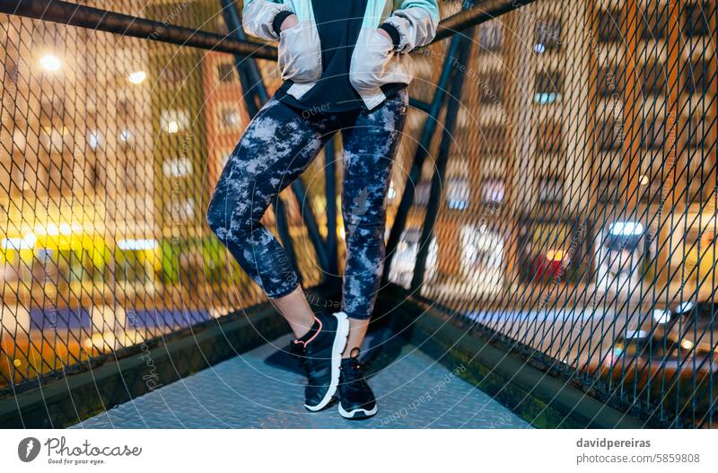 Unrecognizable woman runner wearing sporty leggings and sneakers standing on bridge at night unrecognizable female athlete evening urban city young sportswoman