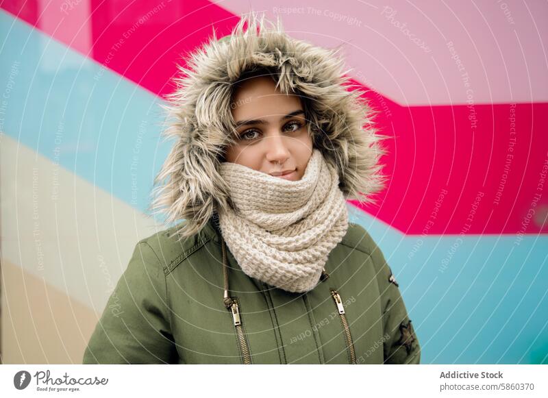 Young woman in cozy winter clothing with colorful background fur trim hood scarf knit smile geometric warm fashion style cold outdoor seasonal portrait female