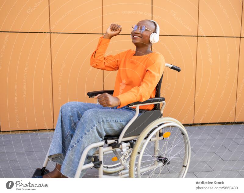 Joyful african american woman in wheelchair enjoying music headphone uplifting outdoor modern orange black woman ethnic enjoyment female mobility accessibility