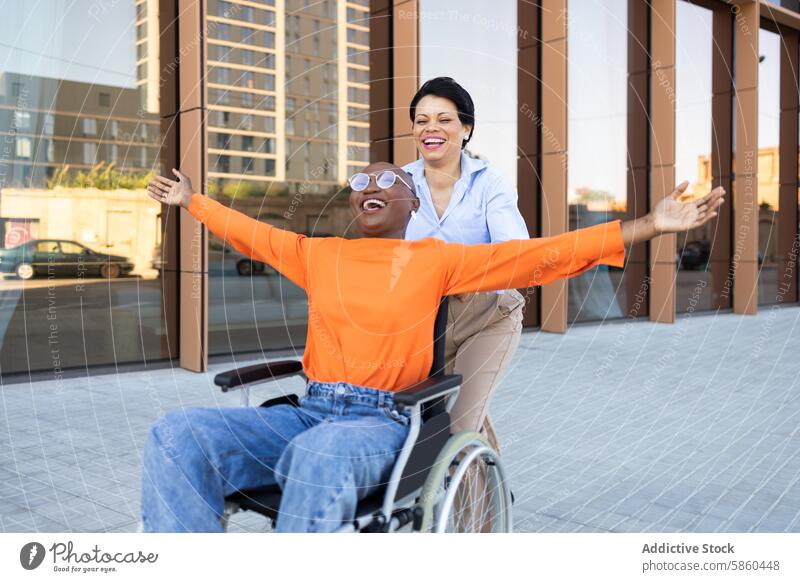 Joyful wheelchair user with assistant enjoying outdoors business urban diversity inclusion accessibility smile happiness sidewalk building city african american