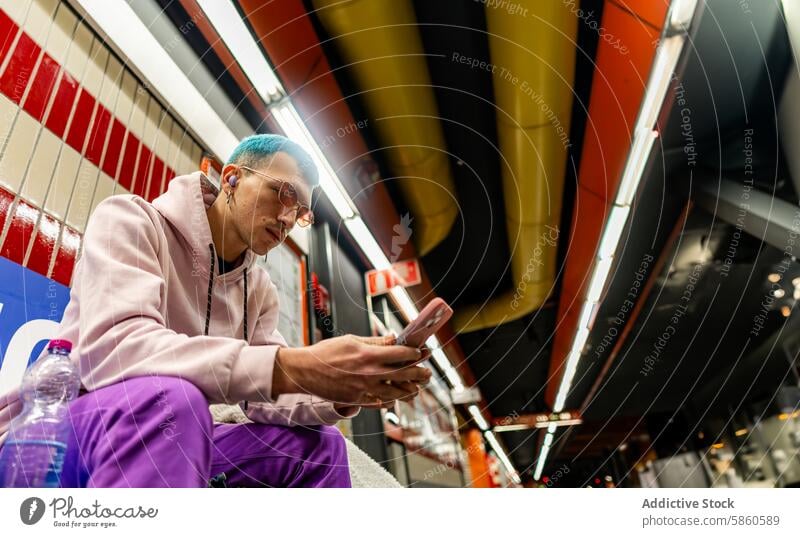 Young man with blue hair using smartphone at subway station young sitting purple outfit colorful platform urban commute technology mobile device casual fashion