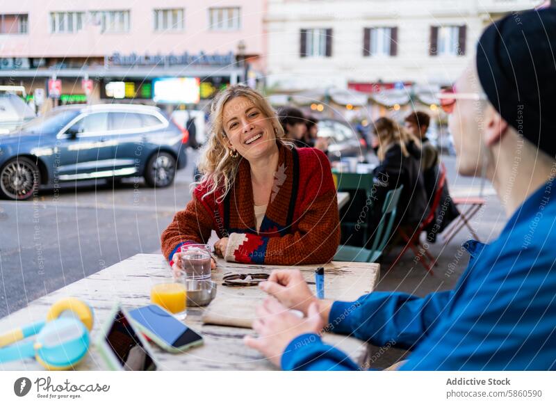 Couple enjoying a cheerful conversation at an outdoor cafe woman smiling urban street table diner car sweater colorful drink juice water sitting talking casual