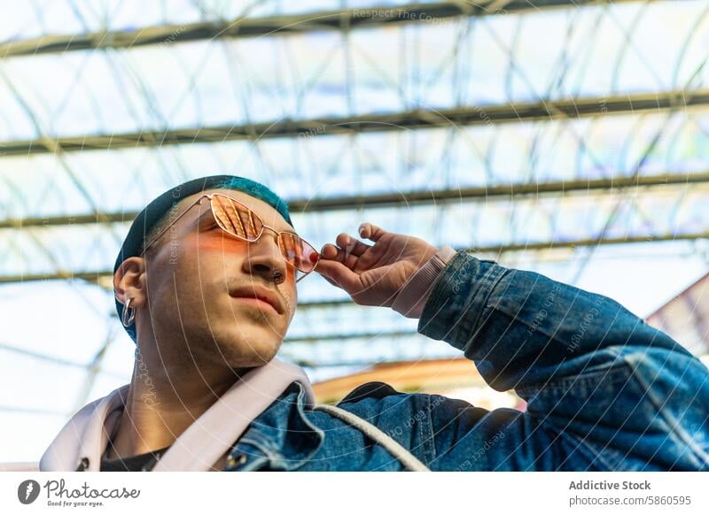 Stylish young man with blue hair and red sunglasses in urban setting trendy stylish city casual sign backdrop sunlight fashion modern youth cool eyewear