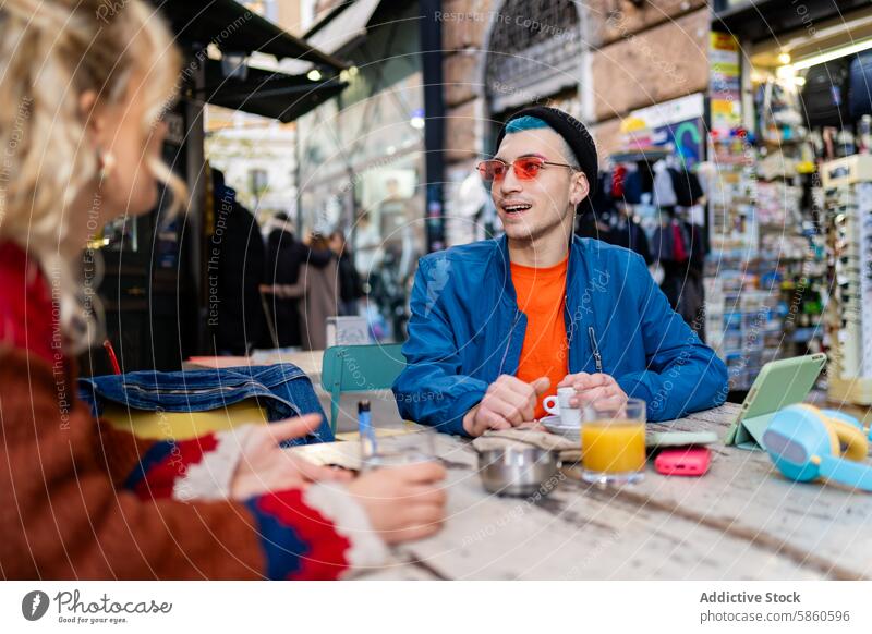 Young man enjoying coffee at a street cafe in the city young outdoor smile digital device book urban table blue hair red sunglasses cheerful daylight
