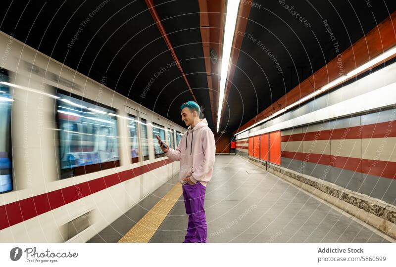 Young man with blue hair using smartphone in subway station young waiting train denim jacket in-ear headphone mobile technology urban casual modern lifestyle