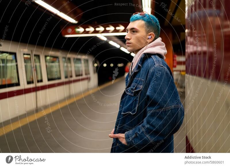 Young man with blue hair waiting at subway station young train nighttime casual denim jacket transportation urban city light public commuter platform rail