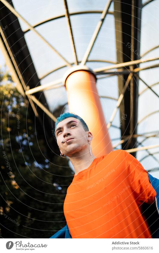 Young man with blue hair in a vibrant orange shirt outdoors young modern stylish geometric architecture background urban fashion male youth bold city lifestyle