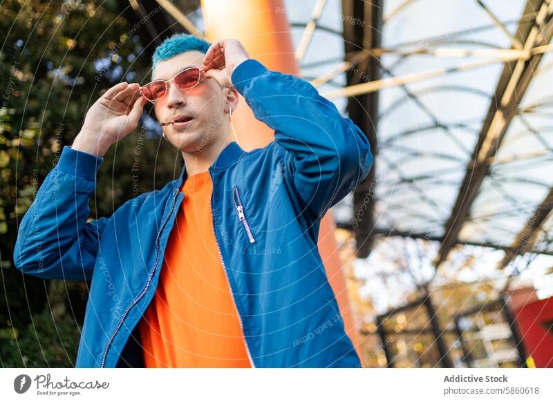 Stylish young man with blue hair adjusting sunglasses outdoors fashion urban style modern orange shirt blue jacket fashionable male city youth trendy casual