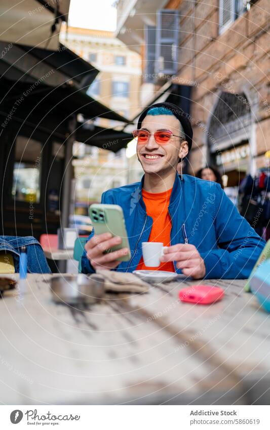 Young man enjoys coffee and smartphone at outdoor cafe young sunglasses urban lifestyle connect cup table smile happy trendy fashion casual sitting technology