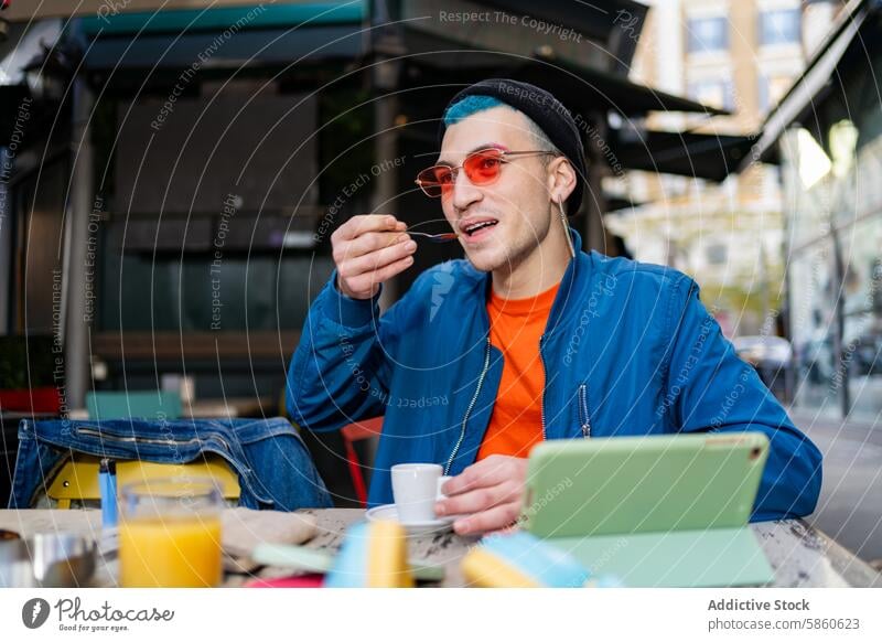 Stylish young man enjoying breakfast at a city cafe eating stylish outdoor tablet espresso blue jacket orange shirt trendy fashion youth urban lifestyle food