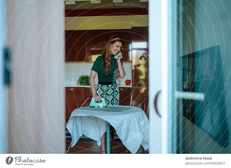 Woman multitasking with ironing and phone call in retro kitchen woman vintage 1950s cheerful domestic scene female adult caucasian smiling smile feminine