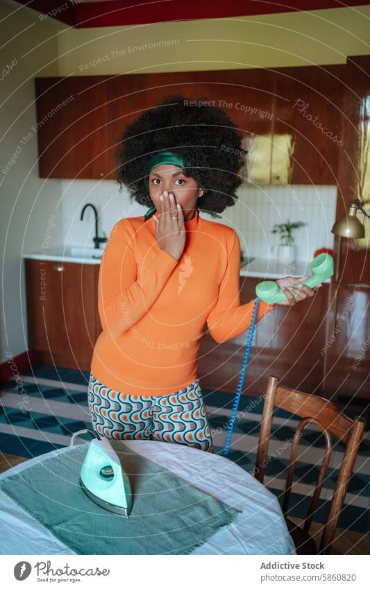 Surprised 1950s housewife with vintage iron and telephone comedy african american woman kitchen surprise looking at camera retro mouth covered expression