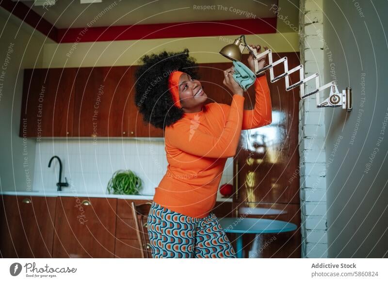 Woman in retro kitchen balancing a lamp humorously woman black afro comical 1950s vintage joyful playful colorful looking up interior home retro style