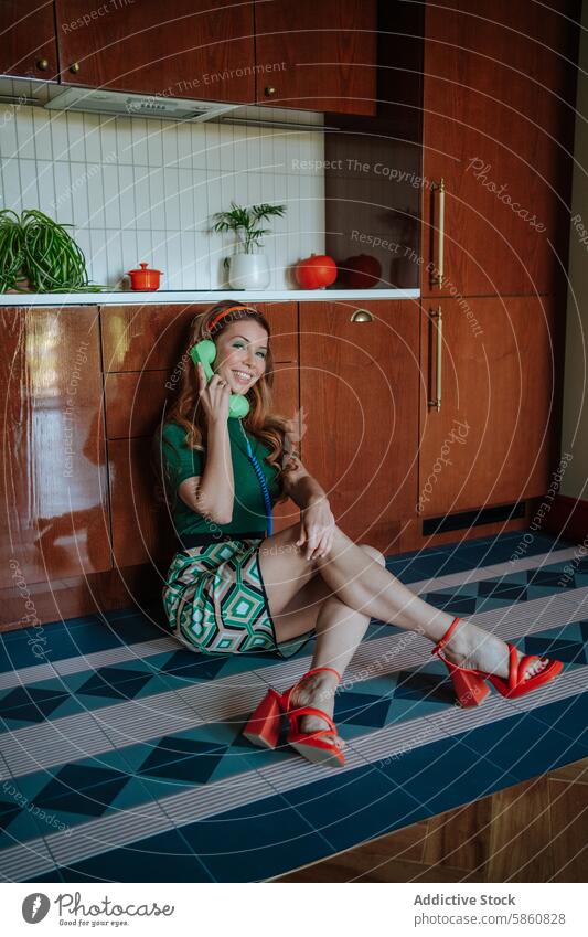 Cheerful retro housewife chatting on phone in a vintage kitchen 1950s woman cheerful telephone talking sitting floor laughing green top patterned skirt orange