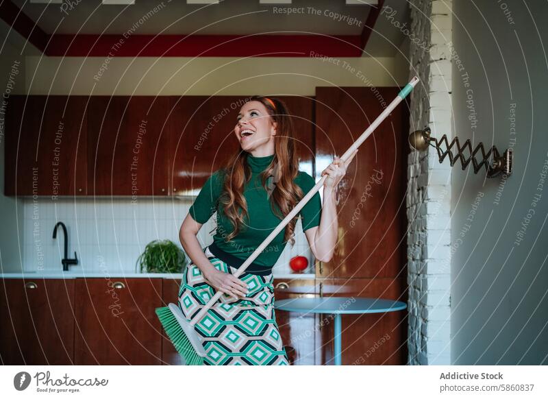 Cheerful 1950s housewife playfully posing with broomstick woman caucasian vintage kitchen looking away green turtleneck cheerful joyful retro fashion style