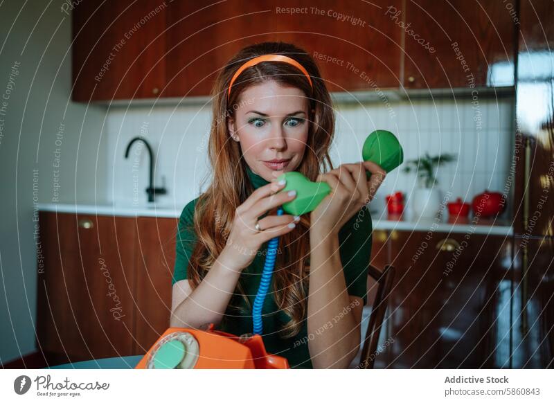 Woman in vintage kitchen using colorful old-fashioned telephone woman 1950s retro redhead playful looking away styled surprised headband amazed astonish