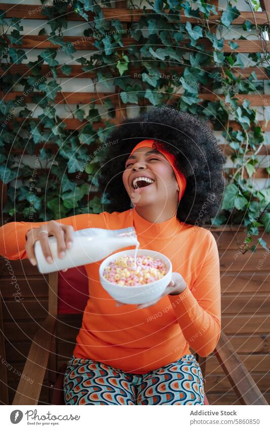 Laughing woman in retro outfit pouring milk into cereal bowl black african american laughing eyes closed afro hair quirky color breakfast vintage headband