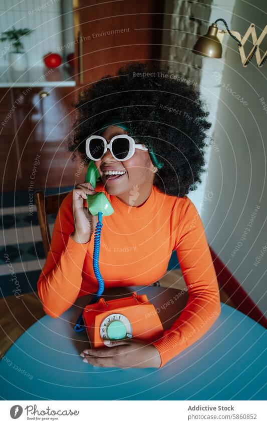 Cheerful woman in retro attire talking on vintage phone 1950s cheerful laughing black rotary dial mid-century modern kitchen orange sunglasses headband seated