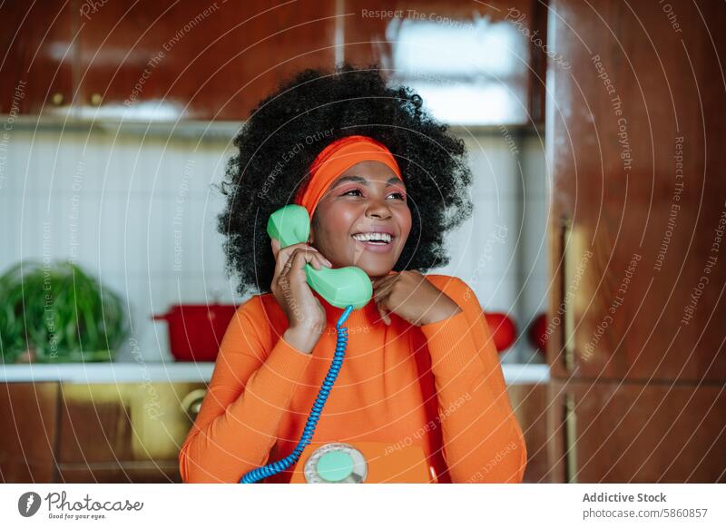 Joyful 1950s-inspired housewife chatting on vintage phone joyful kitchen orange style black african american looking away fashion nostalgia interior