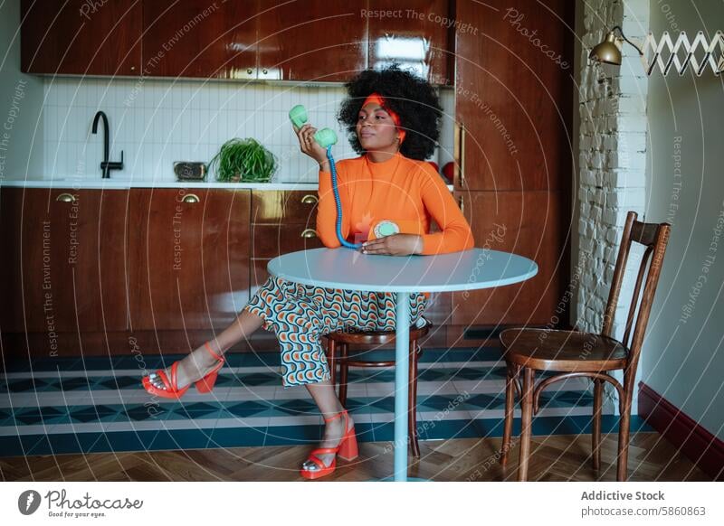 Woman in retro kitchen talking on vintage telephone woman african-american 1950s looking away housewife orange pattern heels chair table faucet playful