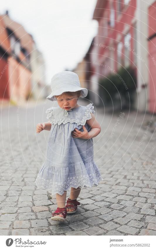A little girl walks dreamily over cobblestones Child Infancy Girl Exterior shot Dress young girl Toddler Summery Dreamily dreaminess Hat Bright Cobblestones