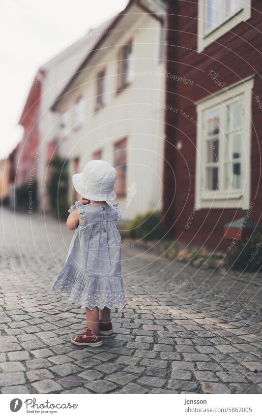 A little girl stands on a cobbled street and looks into the distance Child Infancy Girl Exterior shot Dress young girl Toddler Summery Dreamily dreaminess Hat