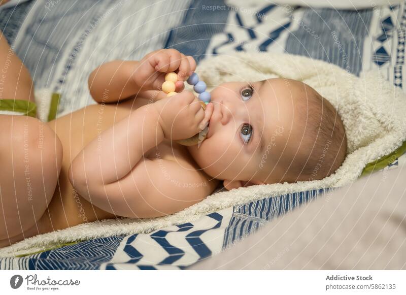 Baby playing with colorful beads on soft blanket baby silicone cozy infant child gaze looking away lying down blue gray white playful texture comfort cute