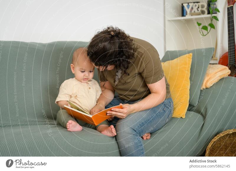 Mother reading to baby while sitting on a couch mother book sofa focused woman child indoor domestic bonding family parenting maternal education learning