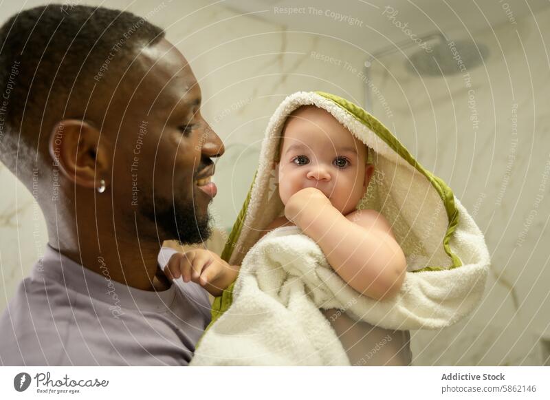 African American father holding his baby in bathroom african american caucasian towel tender moment family bonding infant man child care indoor parenthood