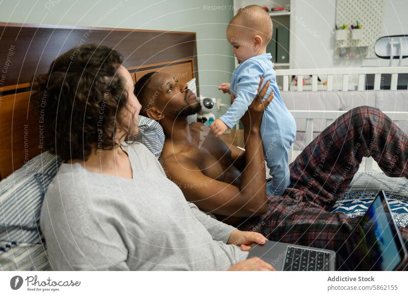 Multiracial family relaxing and playing with baby in bedroom multiracial interracial african american caucasian toddler man woman home bonding joy parenting