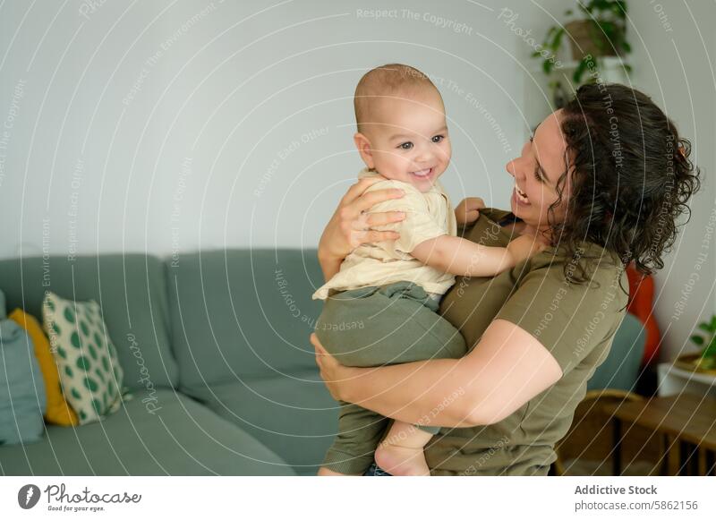 Mother with curly hair holding her baby in living room mother smiling joyful family home indoor happiness child woman parent caring love bonding cheerful