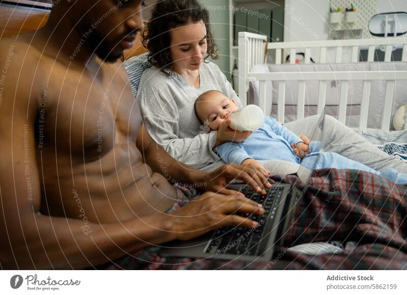 Multiracial family enjoying time together indoors multiracial home african american caucasian baby man woman laptop relaxing feeding baby bottle interaction