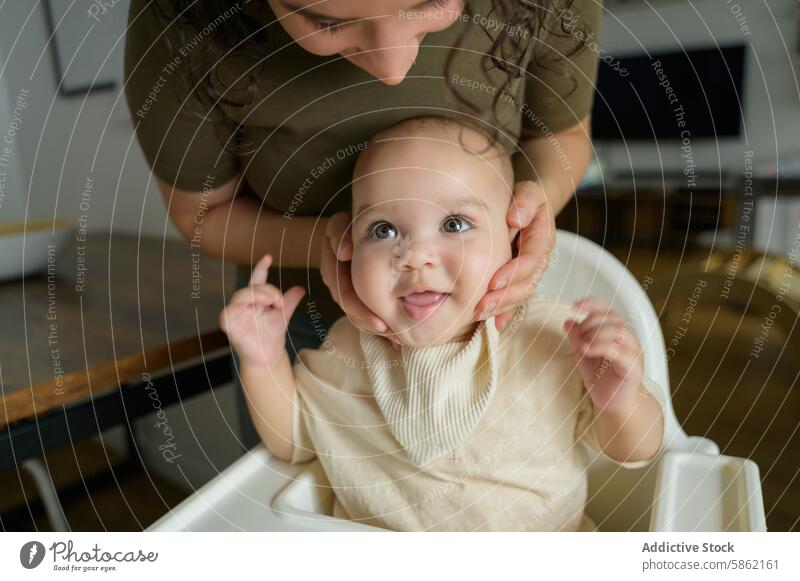 Mother caressing cheerful baby's cheeks at home mother kitchen caucasian family bonding joy happiness pointing female boy childcare nurturing parenting son love
