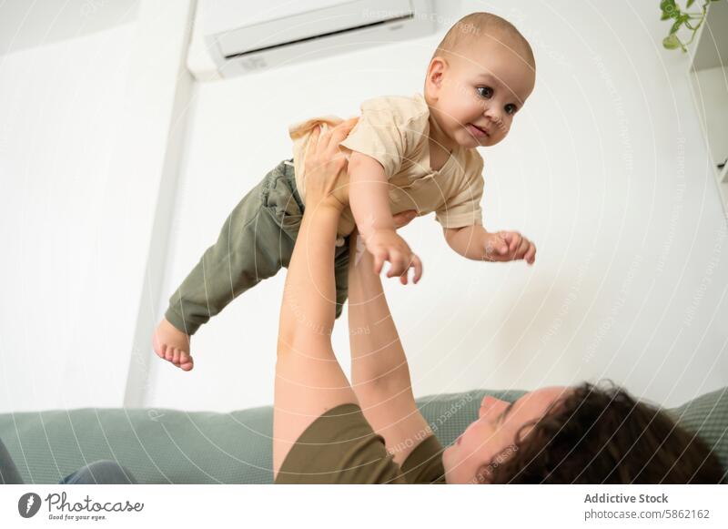 Anonymous joyful mother lifts smiling baby boy in air at home caucasian infant toddler playtime bonding care affection love family female happiness emotion