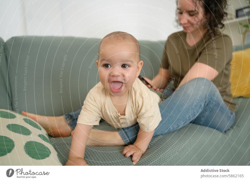 Mother and baby enjoying playful time on couch mother multiracial diverse family sofa mobile phone smiling looking away caucasian indoor home living room