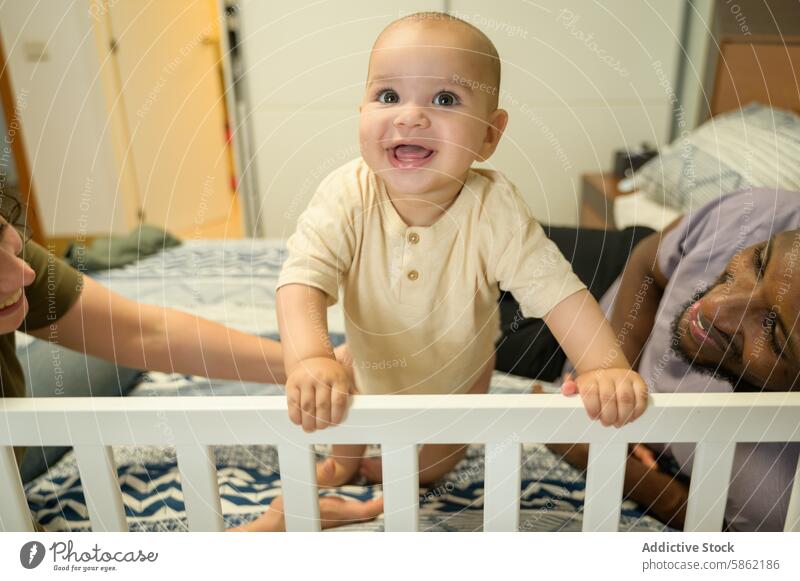 Multiracial family enjoying time with their joyful baby multiracial multiethnic african american caucasian crib smile home happiness child toddler infant parent