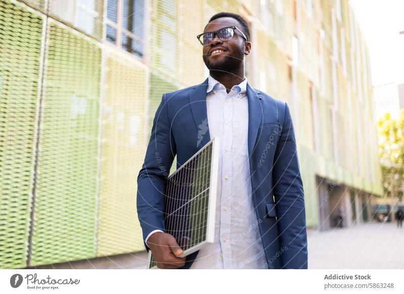 Smiling African American businessman walking with solar panel african american technology innovation sustainable energy urban street professional suit