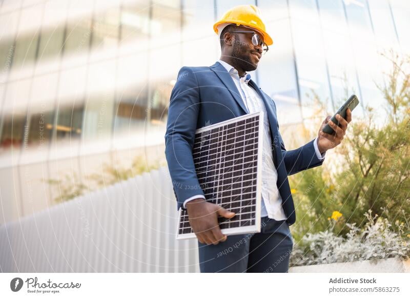 Black business man with solar panel using smartphone african american suit hard hat outdoors technology energy sustainability professional modern connectivity