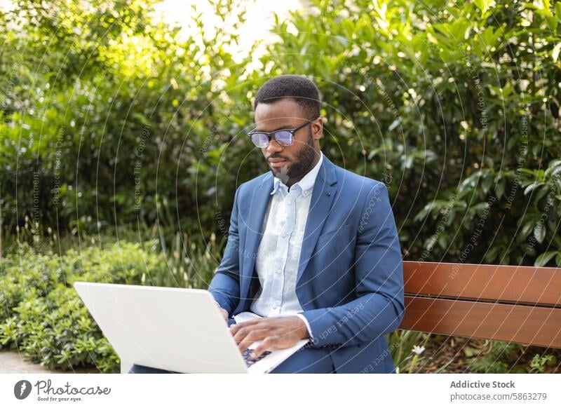 Businessman working on laptop in park setting businessman bench african american professional male remote work technology outdoor nature greenery suit blue suit