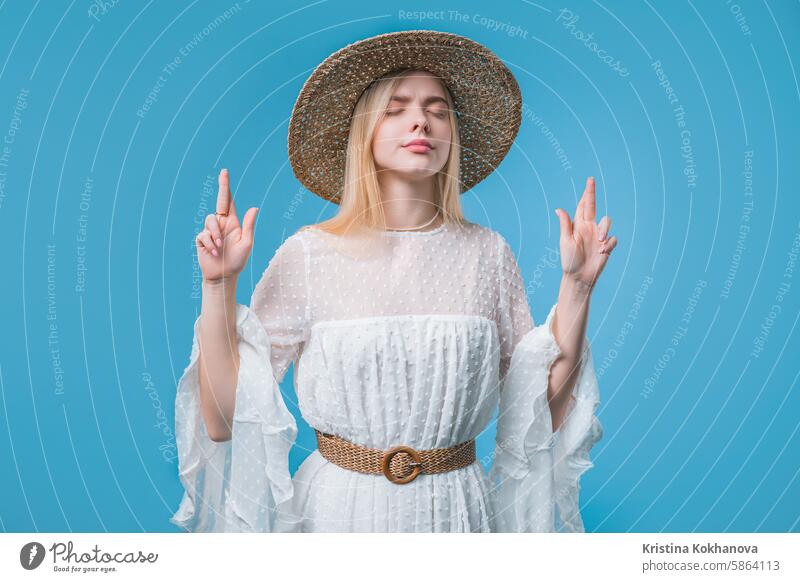 Stylish Woman praying crossed fingers,blue background.Teenager girl begs someone hope prayer hands belief faith god help religion young adult person please